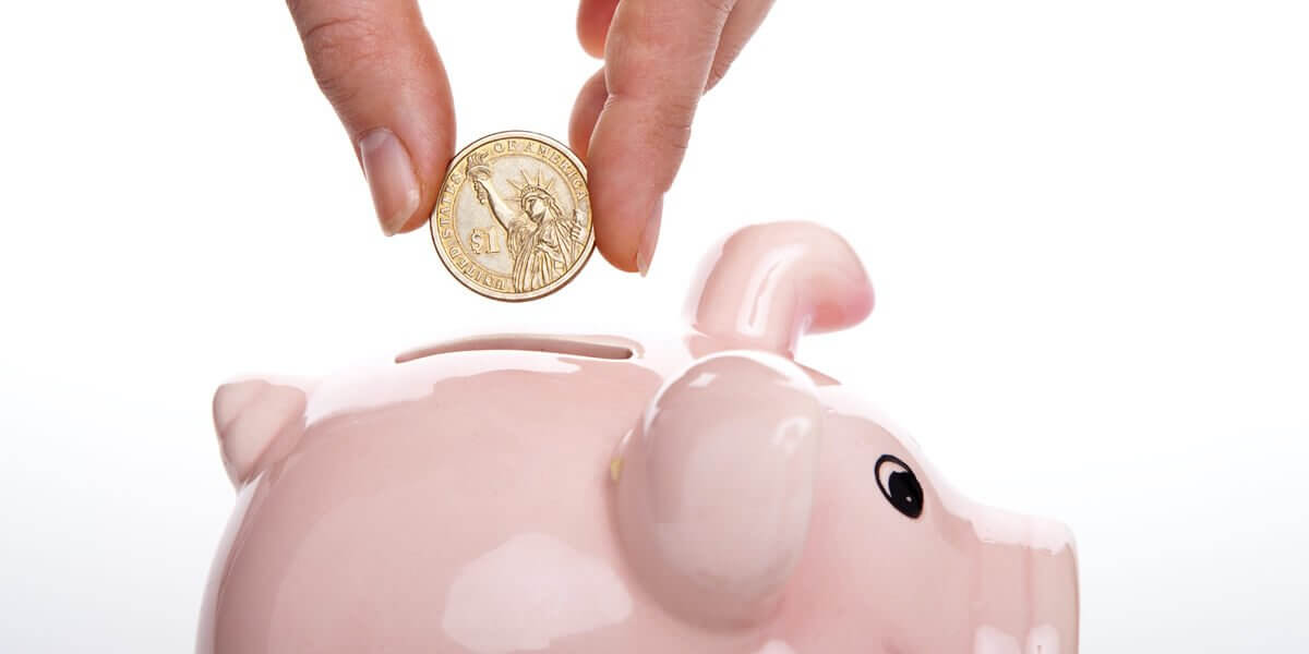 A person putting a coin into a pink piggy bank