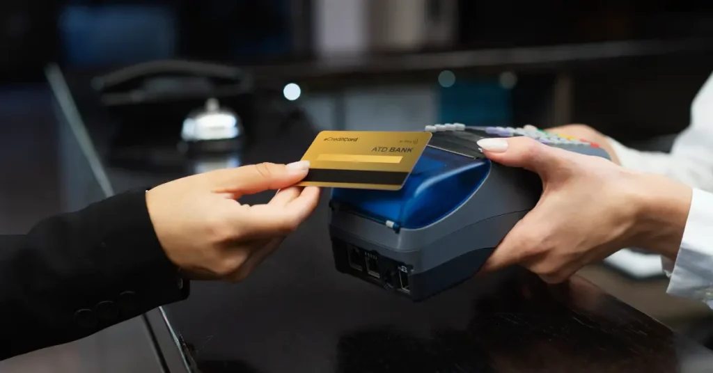 Person inserting a gold credit card into a blue EMV chip reader terminal at a checkout counter.